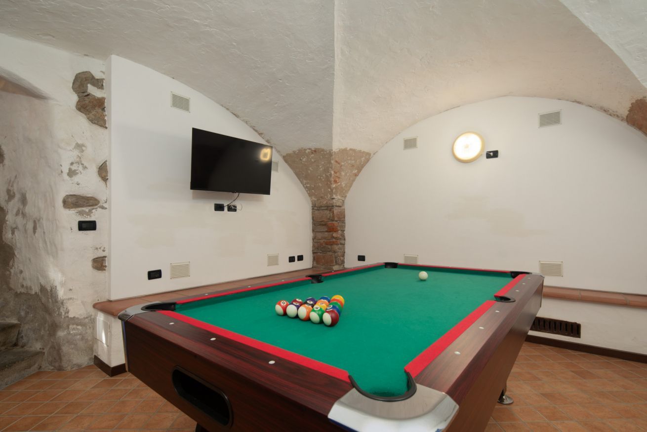 Un tavolo da biliardo con le sue palle, una televisione a muro e un lampadario.
