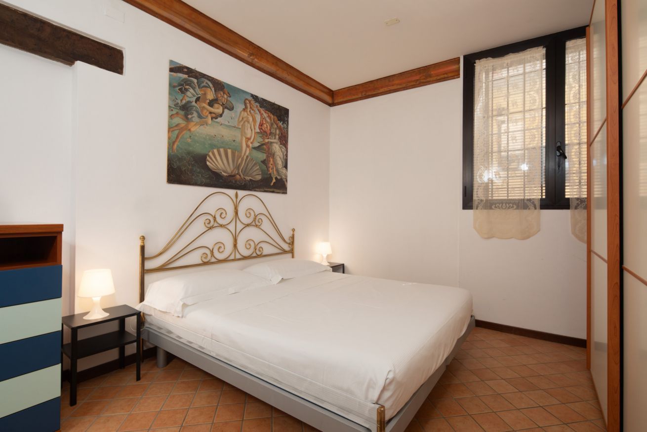 A bedroom with a bed, bedside tables, a painting, and a window with curtains.