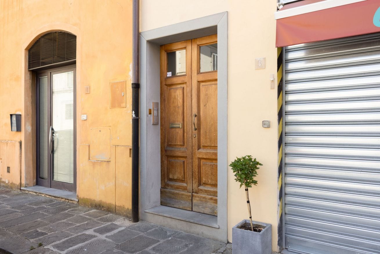 A building with a wooden door, a metal shutter, and a potted plant.