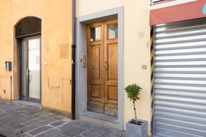 A building with a wooden door, a metal shutter, and a potted plant. - San Frediano Central Stay (Florence)