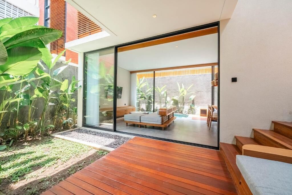 Un interior moderno con cubierta de madera, un vidrio que da a una zona de estar y vistas a un jardín.