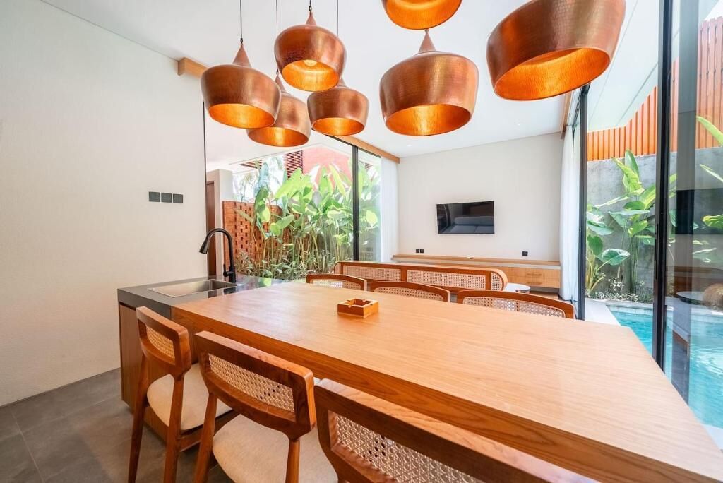 Un comedor moderno con una gran mesa de madera, múltiples sillas y lámparas colgantes de cobre.