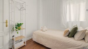 A bedroom with a bed, a white wardrobe, a plant shelf, and a window with sheer curtains. - Apartamento 'Brisa del Sur' para 6 personas, Huelva y Portugal, Wifi, A/C, luminoso (Ayamonte)