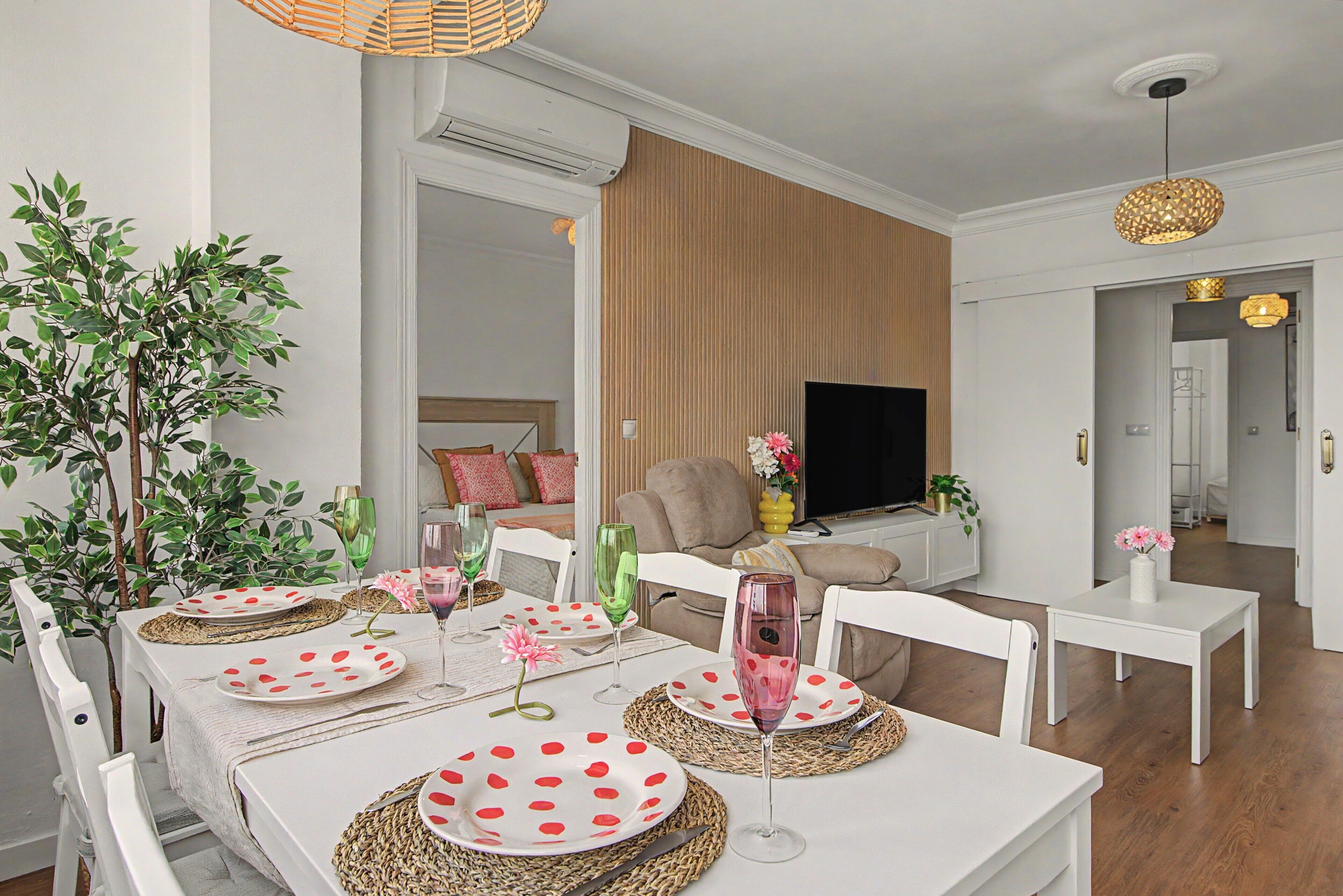 A modern living room with a dining area, a flat-screen TV, and a large plant.