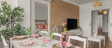 A modern living room with a dining area, a flat-screen TV, and a large plant.