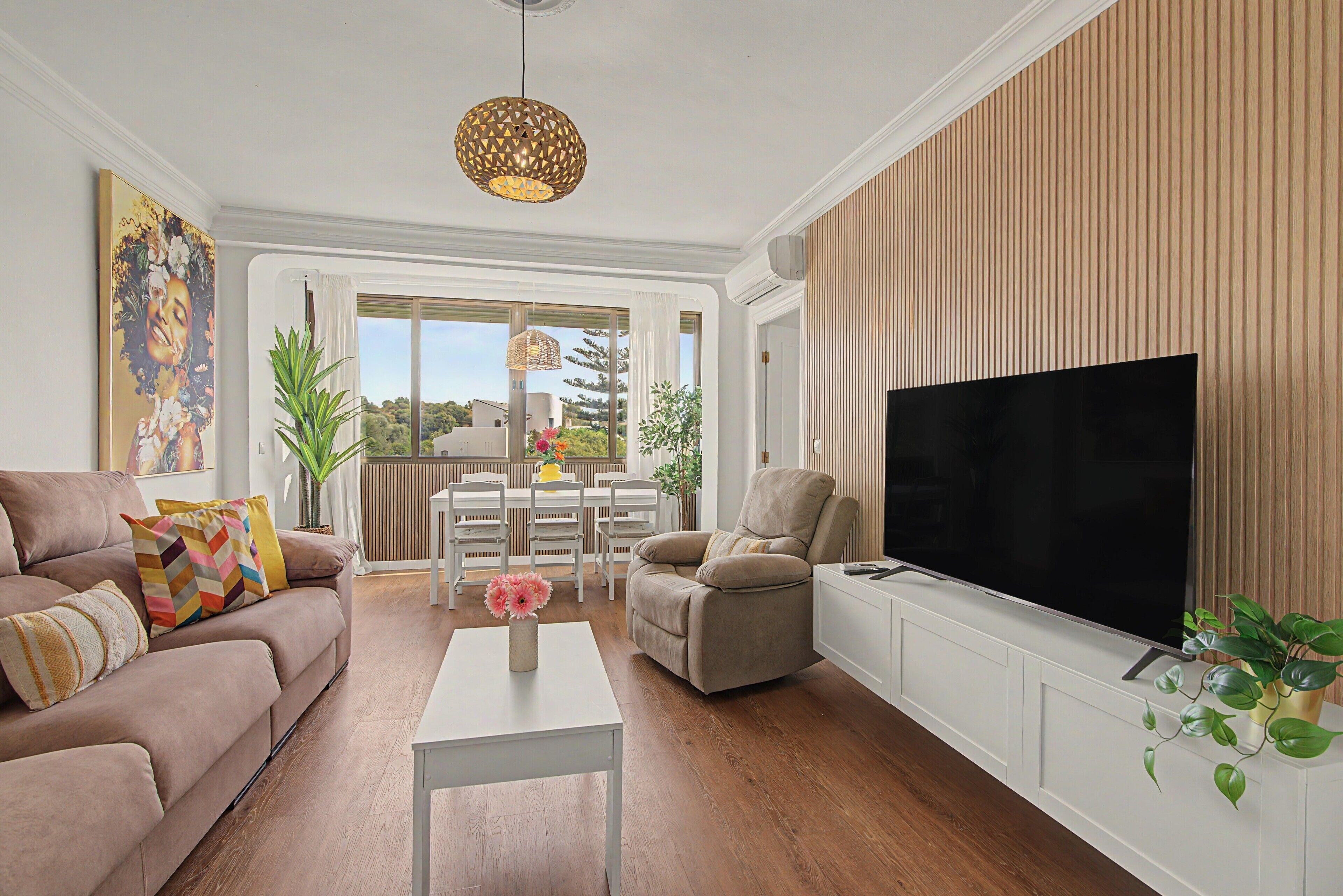 A living room with a sofa, a coffee table, a TV, and a dining area with chairs and a table.