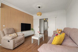 Ein Wohnzimmer mit Flachbildfernseher, zwei Sofas, einem Couchtisch und einer Wand im Holzoptik.