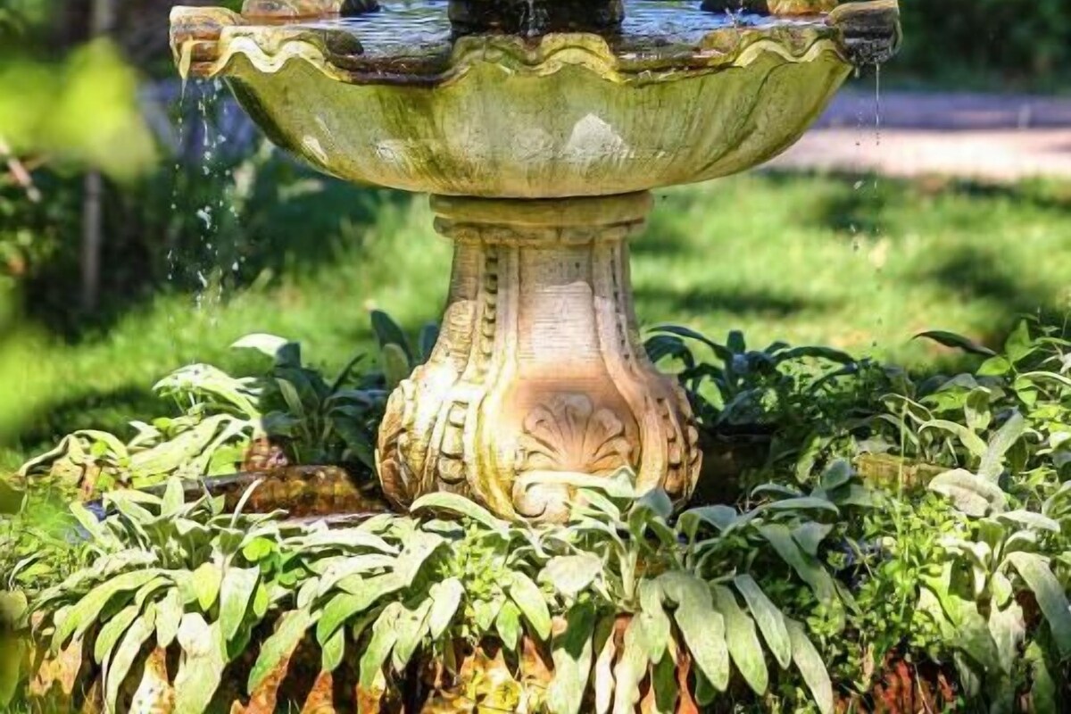 A multi-tiered fountain with statues, surrounded by lush greenery.