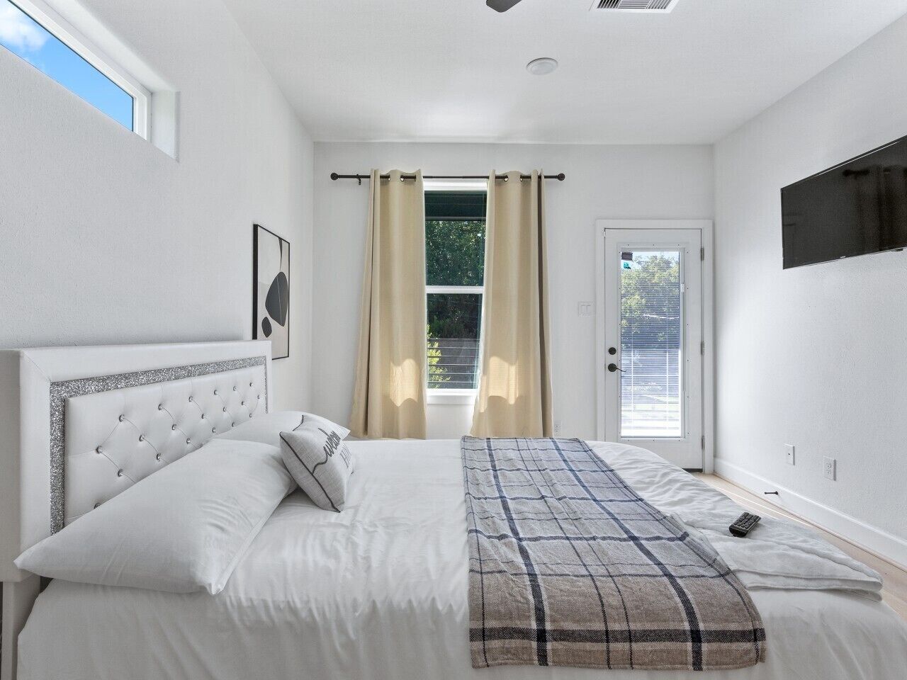 A bedroom with a bed, curtains, a door, and a mounted TV.