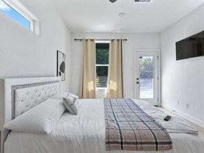 A bedroom with a bed, curtains, a door, and a mounted TV. - Oma Cozy Homes - A Modern, Newly Built Retreat in Houston (Houston)