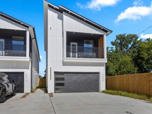 A two-story residential building with a garage, a visible number '7010', and a wooden fence in the background. - Oma Cozy Homes - Modern New-Construction Retreat in Houston (Houston)