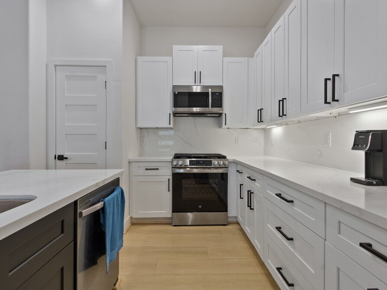 A modern kitchen with white cabinets, stainless steel appliances, and a wooden floor.