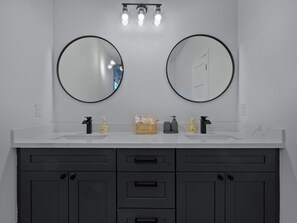A bathroom with two round mirrors, a white countertop, and a dark cabinet with drawers. - Oma Cozy Homes - Modern New-Construction Retreat in Houston (Houston)
