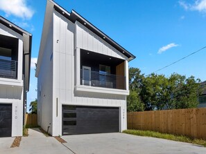 A modern two-story house with a garage, a wooden fence, and a clear sky. - Oma Cozy Homes - A Modern, Newly Built Retreat in Houston (Houston)