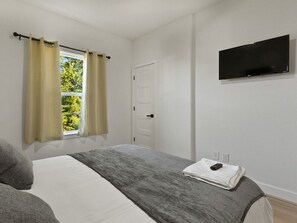 A bedroom with a bed, curtains, a television, and a window with a view. - Oma Cozy Homes - Modern New-Construction Retreat in Houston (Houston)