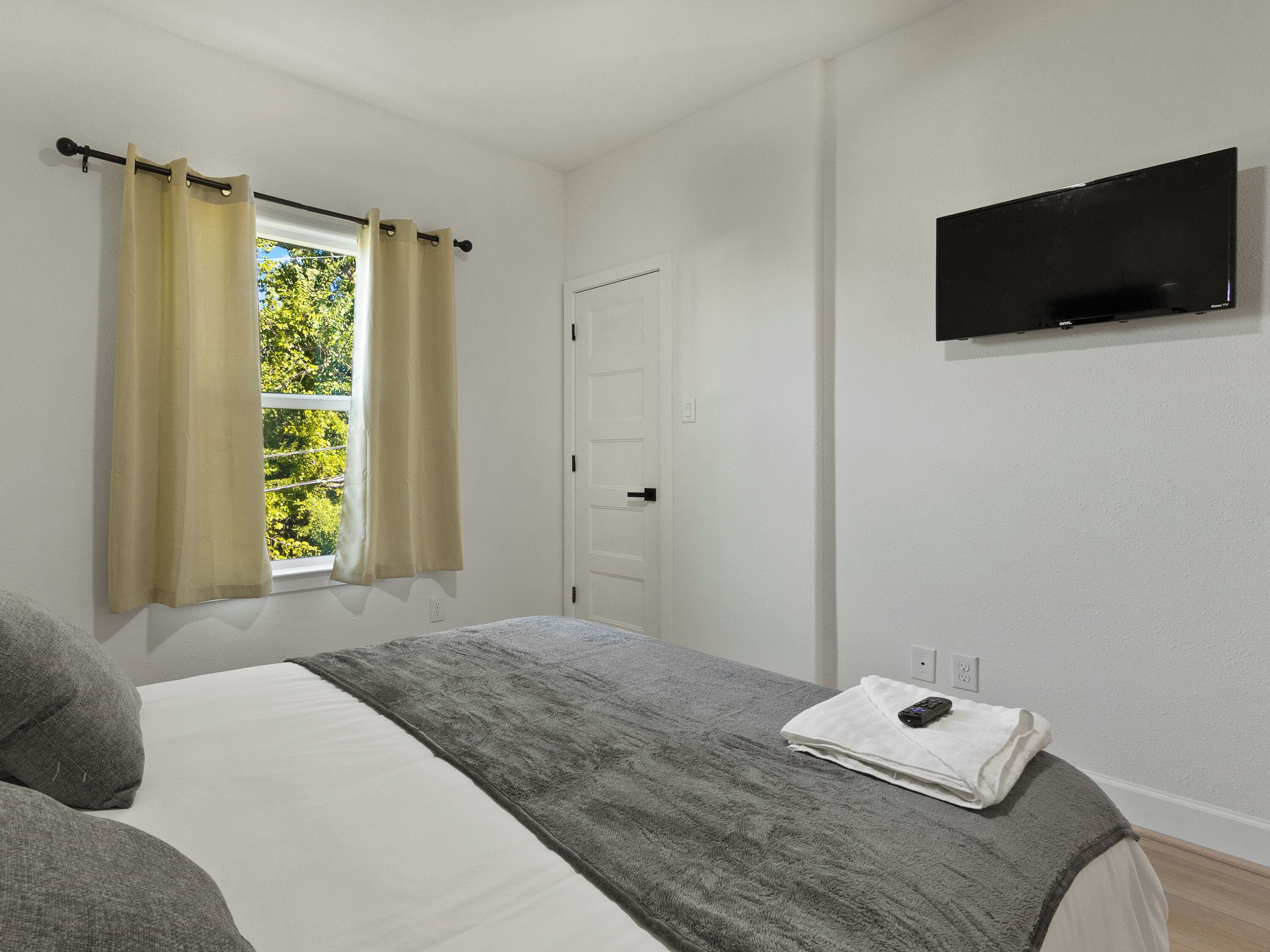Un dormitorio con cama, televisión de pantalla plana, ventana con cortinas y puerta.