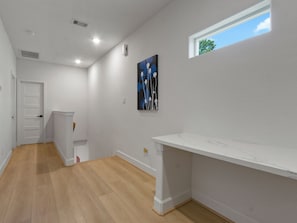 A room with a white door, a white bench, a painting on the wall, and a window with a view of the sky. - Oma Cozy Homes (Houston)