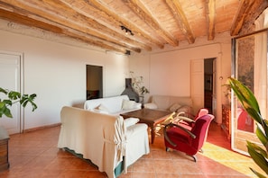 A spacious room with a high ceiling, a white sofa, a red armchair, and a wooden coffee table.