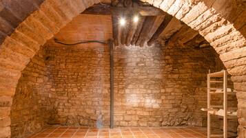 Una habitación con paredes de piedra, suelo de baldosas, una escalera de madera y un tubo de metal.