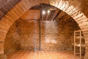 A stone-walled room with a tiled floor, a wooden ladder, and a metal pipe.