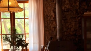 Ein Essbereich mit einem Holztisch, Stühlen, einer Pendelleuchte, einer Vase mit einer Pflanze, einer Steinwand und einem Kamin.