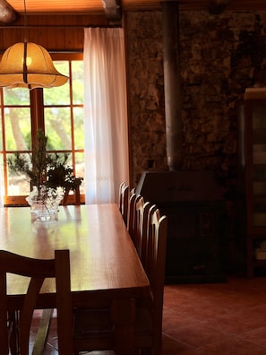 A dining area with a wooden table, chairs, a hanging lamp, a vase with a plant, a stone wall, and a fireplace. - Rural House 'El Masot de Durban' with Mountain Views, Private Terrace and Wi-Fi (Montfalcó Gros)
