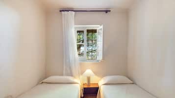Un alojamiento pequeño, de una sola habitación, con dos camas, un ventanal con vistas a árboles y una lámpara de noche.