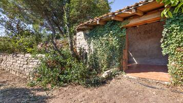 Un bâtiment rustique avec un mur de pierre et des poutres en bois, entouré de verdure et d’arbres.