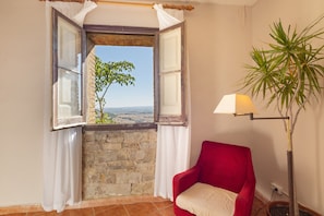 A room with a red chair, a lamp, and a view through an open window.