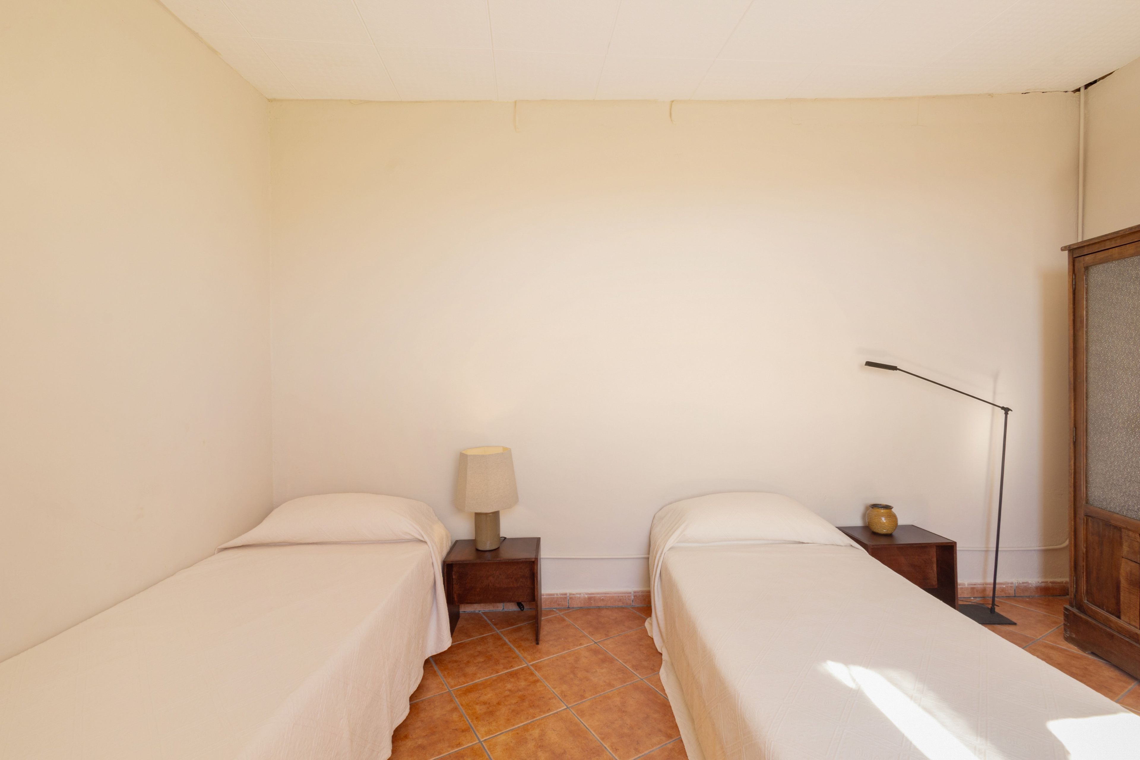 Una habitación sencilla y limpia con dos camas, una mesita de noche con lámpara y una lámpara de pie.