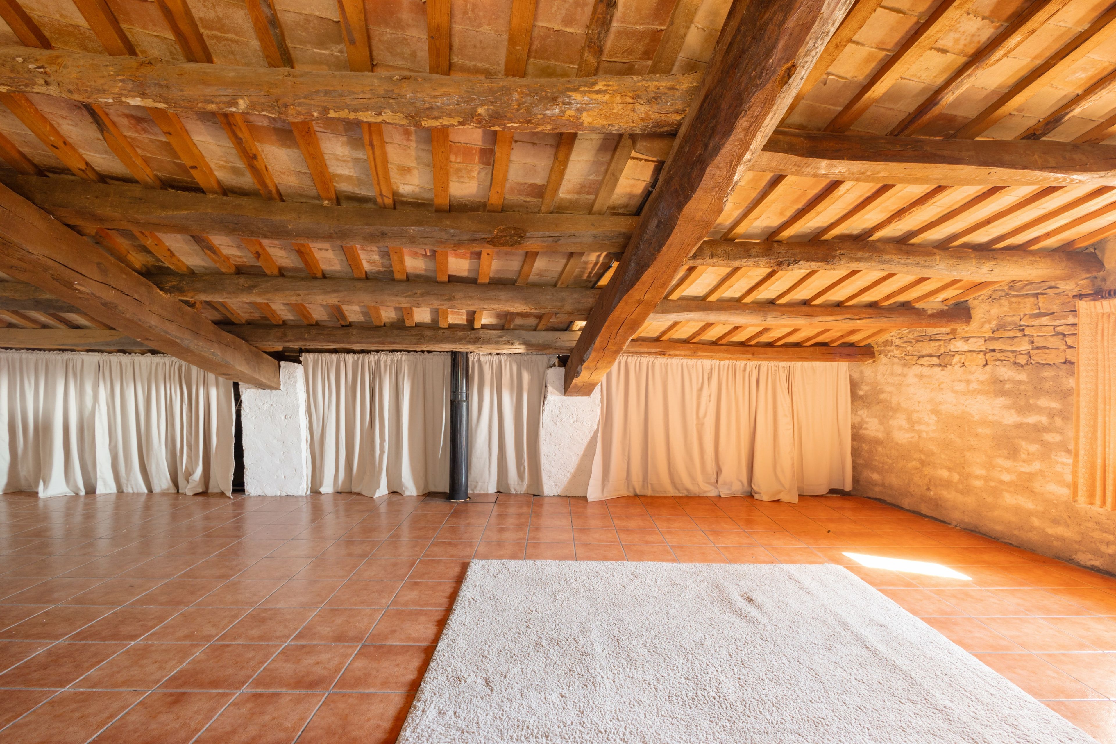Ein geräumiges Zimmer mit hohen Holzbalkendecken, Fliesenboden und einem großen Teppich.