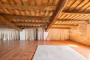 A spacious room with a high wooden ceiling, tiled floor, and a large rug.