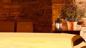 Une pièce avec un mur en pierre, une plante en pot, une table avec une lanterne et une baignoire.