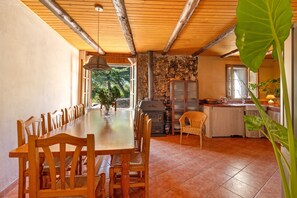 A dining area with a long wooden table and chairs, a stone wall, a fireplace, and a view of the outdoors. - Rural House 'El Masot de Durban' with Mountain Views, Private Terrace and Wi-Fi (Montfalcó Gros)