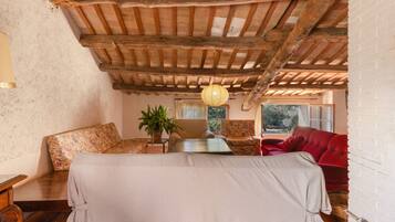 A room with a wooden ceiling, a bed with a white bedspread, a red sofa, and a chair with a floral pattern.