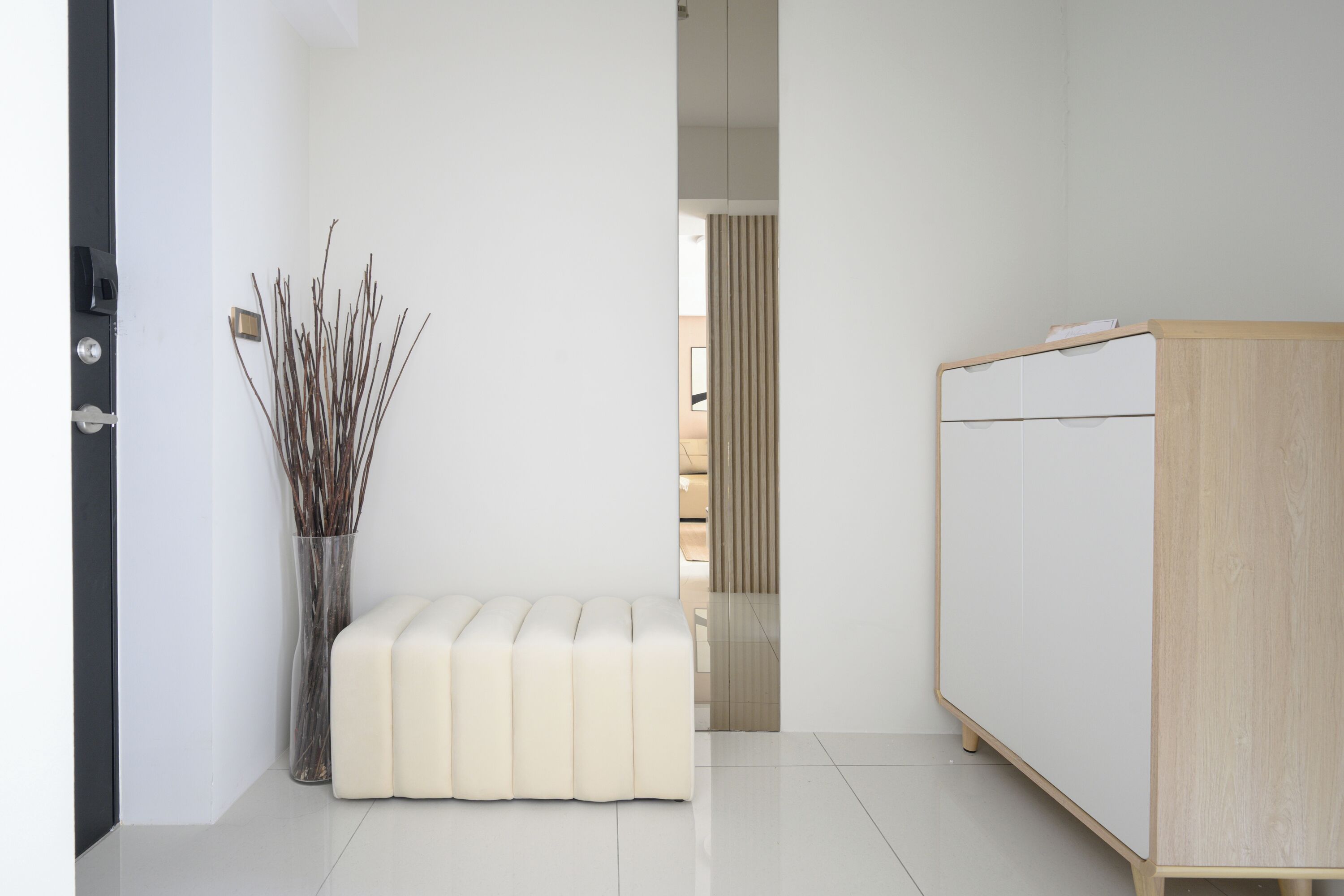 Una stanza minimalista con una panca bianca, un armadio in legno e un vaso con dei rami.