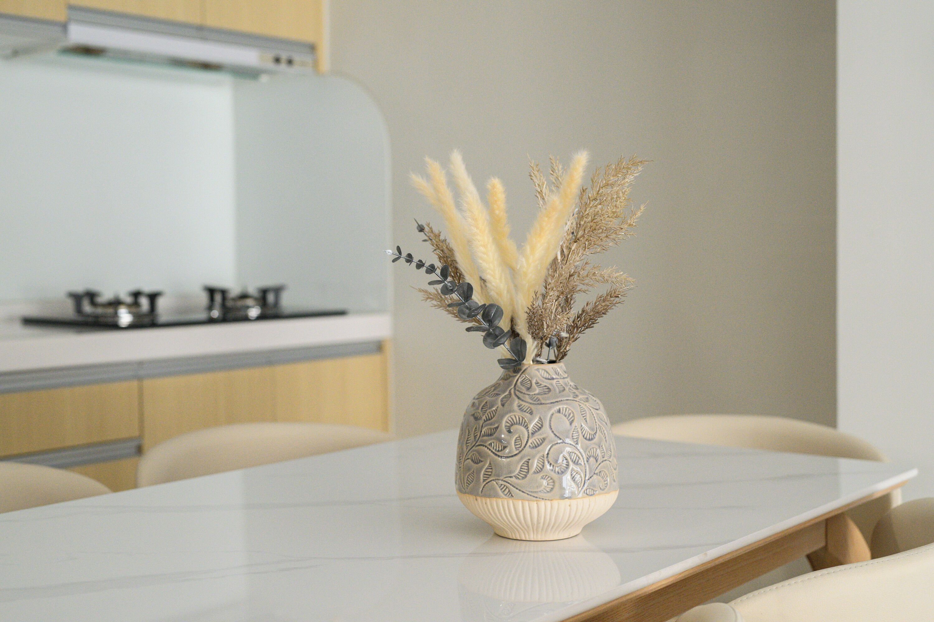A dining table with a vase containing dried plants and a decorative bowl.