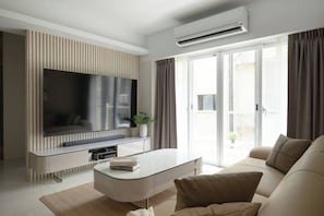 Een moderne woonkamer met een flatscreen televisie, een witte salontafel, een bank en een glazen schuifdeur naar een buitenruimte.