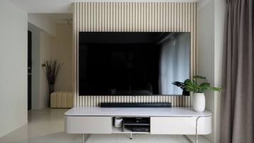 A modern living room with a large flat-screen TV mounted on a wall, a white console table with a plant, and a sofa in the background.