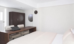 Een slaapkamer met een bed, een bureau met een laptop, een kledingkast en een wandklok.