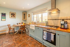 A kitchen with a stove, sink, and washing machine. There are chairs and a table. - Dog Friendly Dorset Escape for 2 (Swanage)