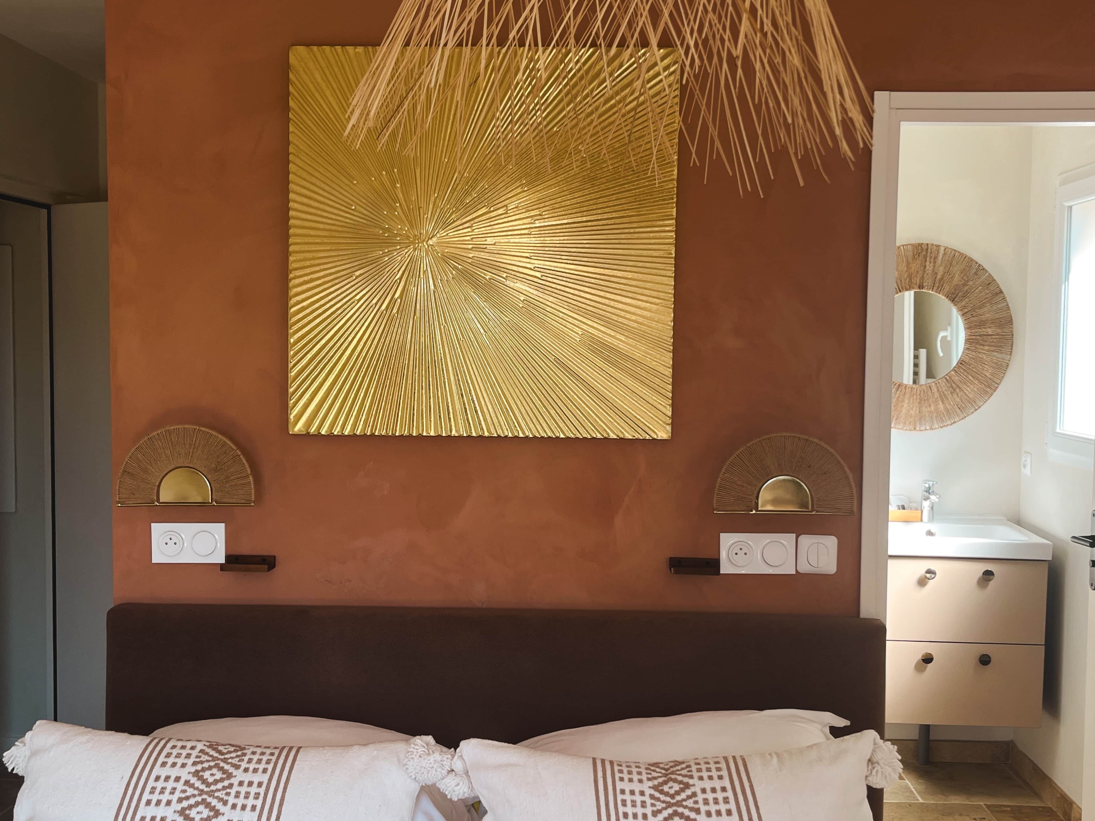 Une chambre à coucher comprenant un lit, un luminaire fixé au mur, un miroir et une prise de courant fixée au mur.