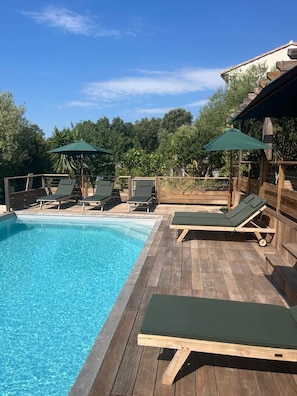Ett trädäck med en swimmingpool, solstolar och parasoller.