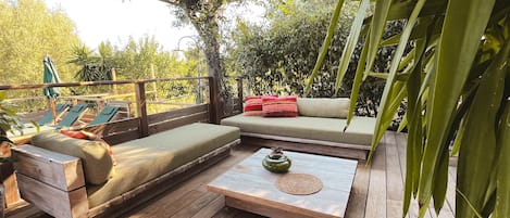A wooden deck with a sofa and a bench, a small table with a vase, and a pergola with climbing plants.