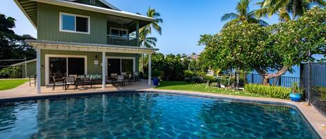 Ein zweistöckiges Haus mit Pool, Gartenmöbeln und einer überdachten Terrasse.