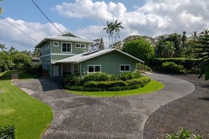 A two-story house with a green exterior, a driveway, and a well-maintained lawn.