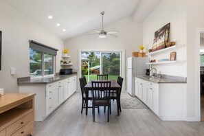 A modern kitchen with white cabinetry, a dining table with chairs, a built-in oven, and a view of the outdoors.