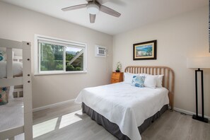 A bedroom with a bed, a window, a ceiling fan, a bedside table, and a nightstand.