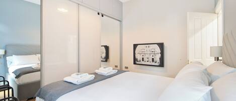 A modern hotel room with a large bed, a bedside table, a chair, and a wall-mounted picture.