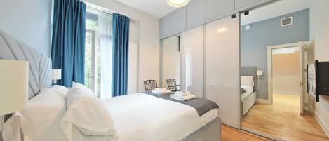 Et moderne soveværelse med en stor seng, et natbord, en stol, et spejl og en garderobe.